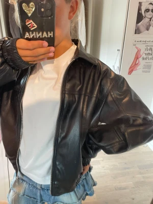 Svart oversized skinnjacka - Snygg svart skinnjacka i oversized modell med dragkedja framtill och klassisk krage. Jackan har breda ärmar och ribbade muddar vid ärmsluten för en cool och avslappnad look. Perfekt att slänga över en t-shirt och jeanskjol för en trendig outfit.