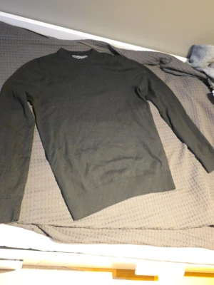 Svart merinoulls tröja. Smått använd. Storlek S - En stilren svart stickad tröja från Selected Homme med rund halsringning och långa ärmar. Tröjan har ribbade muddar vid ärmslut och nederkant. Perfekt basplagg i garderoben och enkel att matcha med olika outfits.