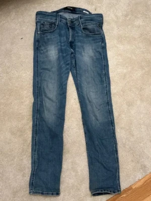 Replay jeans - Säljer ett par blå slim fit jeans från Replay, modellen el Anbass. Jeansen har klassisk femficksdesign, snygga slitningar och tvättade detaljer framtill. Tillverkade i mjukt denimtyg som ger en skön passform och modern look. Säljer pga jeansen kommer till ej användning men annars tycker jag att dessa e riktigt härligt, skit bra skick för priset. OBS PRISET ÄR EJ HUGGET I STENEN