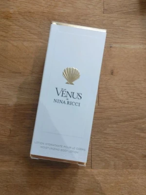 Vénus body lotion från Nina Ricci - Lyxig body lotion från Nina Ricci i serien Vénus. Förpackningen är vit med gulddetaljer och har en elegant snäcksymbol på framsidan. Perfekt för att återfukta huden och ge en fräsch känsla.
