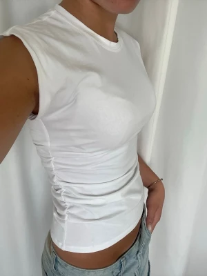 Vit tight t-shirt med rynkade sidor - Säljer en vit, tight t-shirt i bomull med korta ärmar och rund hals. T-shirten har snygga rynkade detaljer på sidorna som ger en cool och modern look. Perfekt till jeans eller kjol för en clean och fräsch stil. Endast änvänd 1 gång❣️