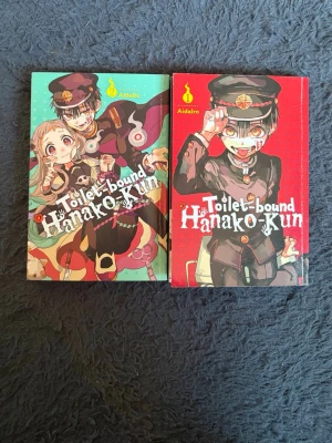 Toilet-bound Hanako-Kun manga vol 1-2 - Två färgglada manga-böcker ur serien Toilet-bound Hanako-Kun av AidaIro. Omslagen har anime-inspirerade illustrationer i rött och turkost med karaktärer i skoluniform. Perfekt för dig som gillar övernaturliga och humoristiska berättelser.