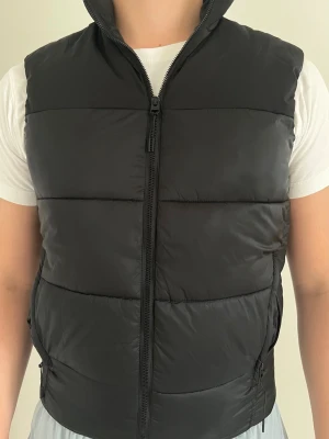 Zara väst - svart, S - Denna svarta väst från Zara är i mycket bra skick och det finns inga synliga tecken på användning. Västen är gjord i nylon och polyester. Två sidofickor med dragkedjeknäppning. Normal passform. Något stor i storleken.