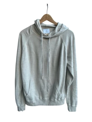 Ljusgrå hoodie med huva och ficka - En stilren ljusgrå hoodie med huva och dragsnören. Hoodien har en klassisk känguruficka framtill och ribbade muddar vid ärmar och nederkant. Tillverkad i mjukt material som känns skönt mot huden. Perfekt för en avslappnad look.