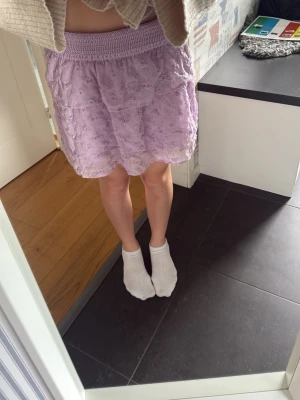 Ljuslila volangkjol med spets - Söt ljuslila kortkjol med volang och spetsdetaljer. Kjolen har bred resår i midjan och ett broderat blommönster, perfekt nu i sommar🩷