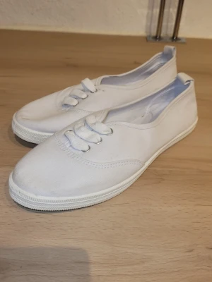 Vita låga tygsneakers - Klassiska vita sneakers i tyg med lågt skaft och vita snören. Skorna har en enkel och clean design med rund tå och vit sula. Perfekta för en avslappnad och stilren look. Helt oanvända. 