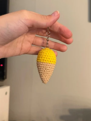 Handvirkad glassnyckelring citron - Säljer en handgjord virkad nyckelring formad som en glass med gul topp och beige strut. Perfekt att hänga på väskan eller nyckelknippan för en söt och unik detalj. Tillverkad i bomullsgarn och polyestervadd.