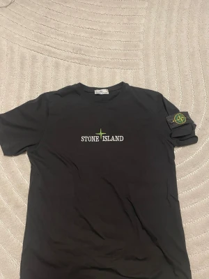 Svart Stone Island t-shirt - Snygg svart t-shirt från Stone Island med klassisk logga på bröstet och ikonisk patch på ärmen. Tillverkad i mjuk bomull och har en normal passform med korta ärmar. Perfekt för dig som gillar streetwear och vill ha något stilrent. Den är barnstorlek XL så skulle säga passar M Och L