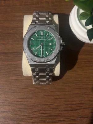 Audemars Piguet Royal Oak  - Snygg Audemars Piguet Royal Oak klocka med grön urtavla och datumvisning. Klockan har en ikonisk åttakantig boett och länkarmband i silverfärgat stål. Perfekt för dig som gillar exklusiv och tidlös design. Priset kan diskuteras!