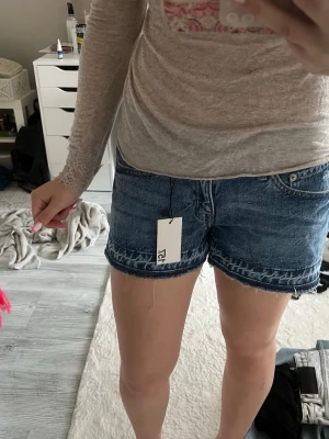 Blå denimshorts från lager - Säljer ett par klassiska blå denimshorts från lager med råa kanter och femficksmodell. Shortsen har normal passform och midja, samt en snygg tvättad look. Perfekta till sommaren och lätta att matcha med olika toppar. sprillans nya endast testade 