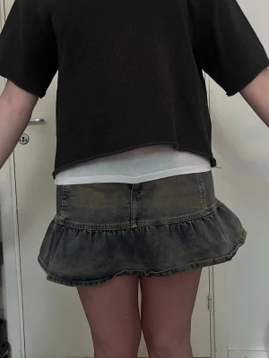 Kort volangkjol i denim - Supersöt kort jeanskjol med volangkant och tvättad look. Kjolen har en klassisk femficksmodell och stängs med dragkedja och knapp framtill. Perfekt för dig som gillar en avslappnad men trendig stil.