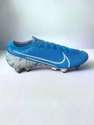 Nike Mercurial vapor 13 - Säljer ett par blå Nike Mercurial fotbollsskor med vit swoosh och grafiskt mönster på hälen. Skorna har låg profil, snörning och ovandel i syntetmaterial för bra bollkontroll. Perfekta för snabba spelare som vill sticka ut på planen.