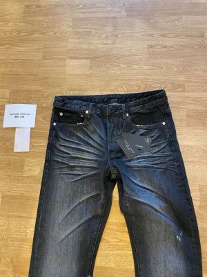 Svarta jeans från Technic Heaven - Snygga svarta jeans från Technic Heaven med raka ben och coola slitningar framtill. Jeansen har klassisk femficksdesign, silverfärgade nitar och etikett på linningen. Materialet är denim med en lätt stretch för skön passform.