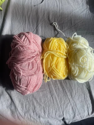 Tre nystan garn i pastellfärger - Säljer tre nystan garn i färgerna ljusrosa, gul och vit. Perfekt för dig som gillar att sticka eller virka egna projekt. Garnet är mjukt och har en klassisk rund form. Passar bra till olika typer av handarbete.