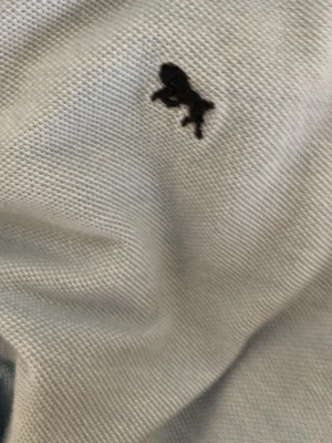 Ljusblå pikéskjorta från L.O.G.G. - Snygg ljusblå pikéskjorta från L.O.G.G. med klassisk krage och knappar framtill. Skjortan har en liten svart broderad logga på bröstet och är tillverkad i mjuk bomull. Perfekt för en clean och avslappnad stil.