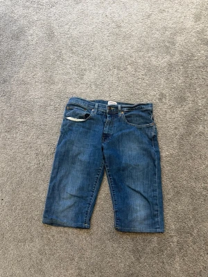 Blå jeansshorts från G-Star RAW - Säljer ett par klassiska blå jeansshorts från G-Star RAW. Modellen har fem fickor, normal passform och är tillverkad i bomull. Perfekta för en avslappnad stil under varmare dagar.