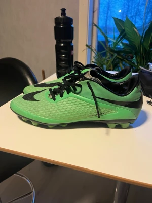 Nike Hypervenom grön - Säljer mina Nike hypervenom. Stl 44. Snygga gröna fotbollsskor från Nike med svart sula och svart snörning. Skorna har en texturerad ovansida för bättre bollkontroll och en stor svart Nike-logga på sidan. På hälen finns en dödskalle-detalj. Perfekta för spel på gräsplan.