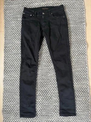 Svarta Nudie Jeans - Säljer nu dessa riktigt snygga Nudie jeans i svart färg🤩💯Storleken är W29 L32 och är mycket bekväma och passar till allt🙌🤩Jeansen är i väldigt bra skick och är väl omhändertagna😁💯Vid frågor och funderingar är det bara att skriva✍️📝