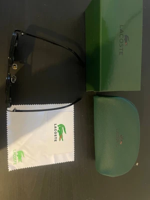 Svarta solglasögon från Lacoste - Snygga svarta solglasögon från Lacoste. Kommer med originalfodral, putsduk och box. Perfekta för dig som vill ha en clean och modern look med en touch av premiumkänsla. Allt orginala tillbehör ingår