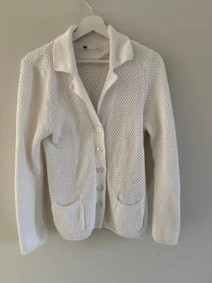 Vit stickad kofta från Flash - Klassisk vit stickad kofta från Flash med strukturmönster, stora ribbade slag och knäppning framtill. Bra skick och i storlek s.