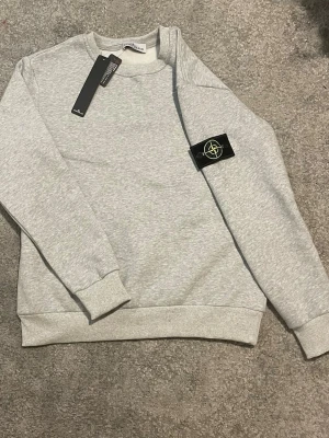 Zara - Snygg ljusgrå sweatshirt från Zara med klassisk rund hals och ribbade muddar vid ärmslut och nederkant. Tröjan har den ikoniska Zara på vänster ärm och är tillverkad i mjukt bomullsmaterial.