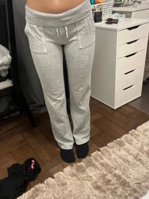 Grå mjukisbyxor Juicy Couture XS - Mysiga grå mjukisbyxor från Juicy Couture med bred midjeresår, dragsko och stora fickor framtill. Byxorna har rak passform och är tillverkade i mjukt sweatshirtmaterial som är perfekt för chill dagar.