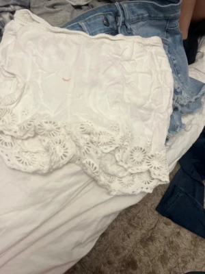 Vita shorts med spetsdetaljer - Säljer ett par vita shorts med bred spetskant längst ner. De har en avslappnad passform och elastisk midja för extra komfort. Perfekta till sommaren och ger en fräsch och feminin look. Materialet känns lätt och luftigt. Smink fläck som inte går bort 