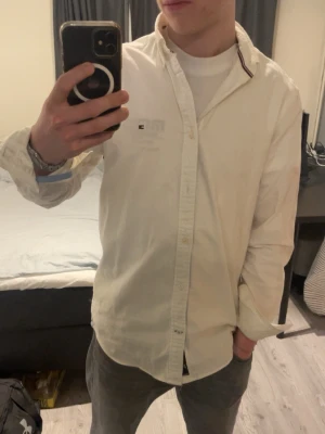 Vit slim fit skjorta Tommy Hilfiger - Snygg Tommy hilfiger skjorta i vitt med blåa detaljer invändigt. Saknar en knapp ner till, men ingen som förstör användningen. Passar perfekt med en vit T-shirt under. Bara höra av sig vid frågor! 