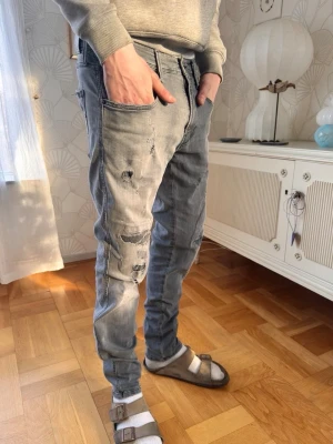 Feta Replay jeans med slitningar  - Säljer ett par grå jeans med skinny fit och slitningar på framsidan. Jeansen har klassisk femficksmodell, låg midja och detaljerade sömmar på bakfickorna. Perfekta för en avslappnad och trendig look.