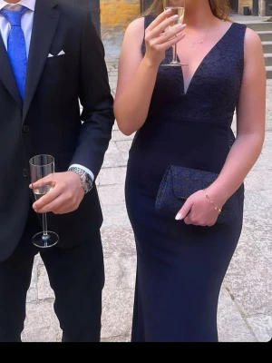 Marinblå balklänning med spets - Elegant marinblå balklänning med v-ringning. Överdelen har fina spetsdetaljer och klänningen har en figurnära passform som framhäver siluetten. Köpt på Zalando från märket Wal G. Perfekt för bal eller festliga tillfällen. Endast använd en gång🫶 priset är inte hugget i sten hör gärna av er!