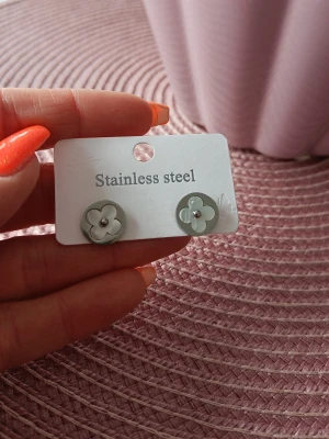 Blommiga örhängen i rostfritt stål - Nya Snygga örhängen i form av blommor i silverfärgat rostfritt stål. De har en stilren och enkel design med en liten pärldetalj i mitten av varje blomma. 