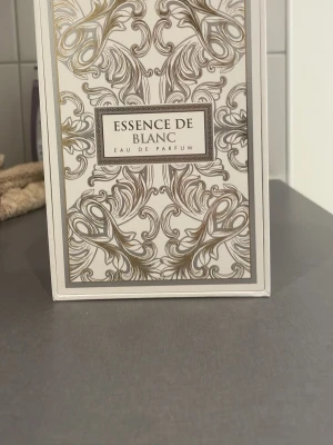Essence De Blanc Eau de Parfum 100ml - Essence De Blanc Eau de Parfum från Fragrance World kommer i en elegant vit och guldmönstrad förpackning. Doften har fräscha toppnoter av citron, apelsin och bergamott, kryddiga hjärtnoter av neroli, kanel och ingefära samt basnoter av svart te, ambroxan, guaiac-trä och olibanum.