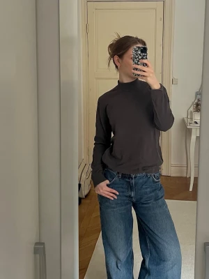 Mörkgrå polotopp i bomull - En enkel och stilren mörkgrå polotopp med lång ärmar.  Perfekt att matcha med jeans eller kjol för en avslappnad vibe.