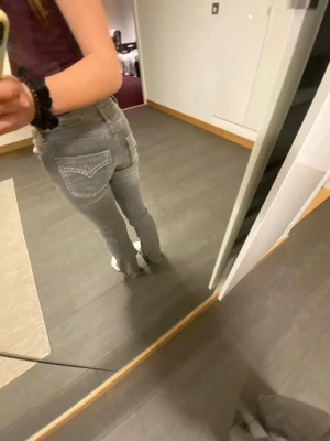 Gråa raka jeans med kontrastsömmar - Säljer ett par gråa jeans med raka ben och tydliga vita kontrastsömmar på bakfickorna. Jeansen har klassisk femficksdesign och normal midja. Perfekta för en avslappnad och trendig look.