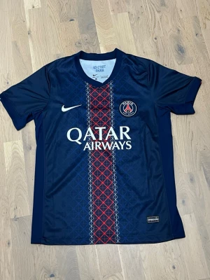PSG matchtröja Nike blå - Säljer en blå Paris Saint-Germain matchtröja från Nike med Qatar Airways som sponsor. Tröjan har ett mönstrat rött och vitt band i mitten, PSG-logga på bröstet och Nike-logga. Materialet är lätt och andas, perfekt för fotboll eller träning. Från litbuy 