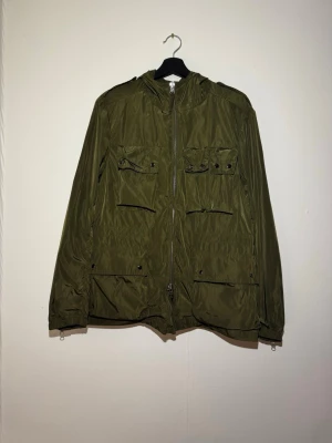 Gant field jacka - Snygg olivgrön jacka/field jacka i lättviktigt material med fyra framfickor och dragkedja. Jackan har huva och justerbar nederkant, perfekt för lager på lager. Passar dig som gillar en clean och funktionell stil.