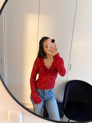 Röd spetsblus med v-ringning - Snygg röd långärmad blus i spets med v-ringad hals och blommigt mönster. Perfekt att styla med jeans eller kjol för en trendig look. Transparent material som ger en cool vibe.