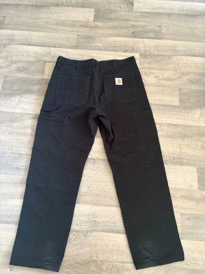 Svarta Carhartt Double Knee cargobyxor - *Pris kan diskuteras* Säljer ett par svarta Carhartt Double Knee cargobyxor med raka ben och flera praktiska fickor. Tillverkade i 100% bomull med slitstarka förstärkningar över knäna. Klassisk Carhartt-logga på bakfickan och robust känsla. Perfekta för dig som gillar streetwear. Nästan helt nya förutom lite missfärgning på botten av byxorna nära fötterna, säljer för att dem är alldeles för stora för mig. 