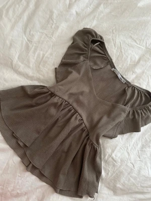 Beige volangtopp med v-ringning - Supersöt beige topp med v-ringad hals och volangdetaljer på både ärmar och nederkant. Toppen har korta ärmar och är tillverkad i ett mjukt, lätt material som ger en flowy känsla. Perfekt för dig som gillar romantiska och feminina plagg.