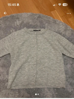 Ljusgrå kofta från 157 - Mysig ljusgrå kofta från 157 med rund halsringning och pärlknappar framtill. Koftan har långa ärmar och ribbade muddar vid ärmslut och nederkant. Perfekt att slänga över en t-shirt för en chill look.