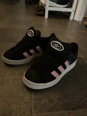 Svarta Adidas campus sneakers med rosa ränder - !!rengörs innan jag skickar dom!! Använda någon gång men är  fortfarande i toppkvalitet! Går att buda ner .säljer på grund av att dom är för små