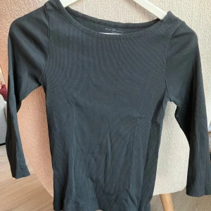 Jennie Top från Brandy Melville NY  - En svart långärmad topp från Brandy Melville i ribbad bomull. Toppen har en rund halsringning och sitter tight mot kroppen, perfekt för att styla med jeans eller kjol. Enkel och stilren design som passar till många olika looks.