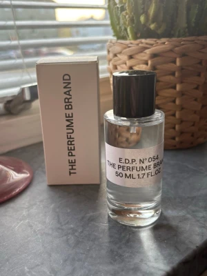 The Perfume Brand E.D.P. N°054 50ml - En stilren parfym från The Perfume Brand, E.D.P. N°054. Flaskan är cylindrisk i genomskinligt glas med svart plastlock och enkel vit etikett. Volymen är 50 ml. Kommer i en vit kartong med minimalistisk design. Ny, dupe på another 13 av le labo. 