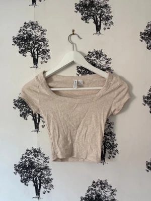 Beige croppad ribbad topp H&M - Säljer en ljusbeige croppad topp från H&M med ribbad struktur. Toppen har korta ärmar och en bred, rundad urringning som ger en snygg och avslappnad look. Perfekt att matcha med höga jeans eller kjol.