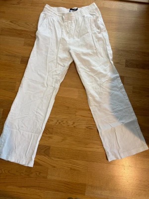 Vita linnebyxor - Säljer ett par vita linnebyxor med resår i midjan och snörning. Byxorna har raka ben, sidofickor och en bakficka. Tillverkade i luftigt linnetyg som ger en chill vibe och passar perfekt till sommaren.
