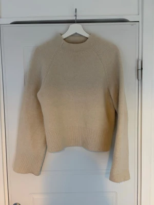 Beige stickad tröja från H&M - Mysig beige stickad tröja från H&M i ullblandning. Tröjan har en rak passform, ribbade muddar och hög hals. Perfekt för kalla dagar och enkel att matcha med olika outfits.