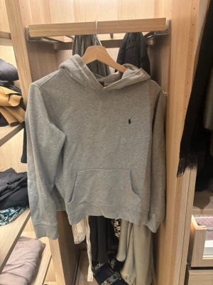 Grå hoodie från Polo Ralph Lauren - Snygg grå hoodie från Polo Ralph Lauren med klassisk huva och känguruficka. Diskret logga broderad på bröstet i mörkblått. Tillverkad i mjuk bomullsblandning som känns skön mot huden. Perfekt för en avslappnad och stilren look. Nypris c 1200