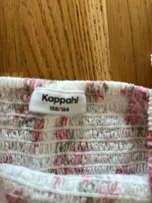 Blommig topp med puffärm från Kappahl - Supersöt topp från Kappahl med vita och rosa blommor, smockad kropp och stora puffärmar. Toppen har en fyrkantig urringning och volangkant nedtill. Perfekt för dig som gillar romantisk och trendig stil.