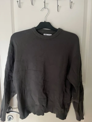 Mörkgrå stickad tröja från Zara - Mörkgrå stickad tröja från Zara med rund halsringning och ribbade muddar vid ärmslut och nederkant. Tröjan har en enkel och clean design som passar perfekt till lager på lager och är tillverkad i mjukt material.