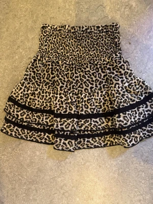 Leopardmönstrad kortkjol med volanger - Snygg kortkjol med leopardmönster och bred smock i midjan. Kjolen har volanger och svarta banddetaljer👌🏼 , kommer dock inte till användning för att den inte passar längre 🙌🏽
